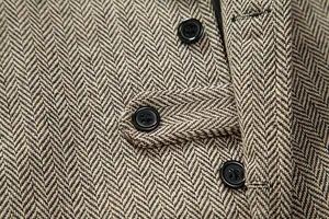 Primo piano del tessuto tweed marrone a spina di pesce e dei bottoni di un gilet da uomo.