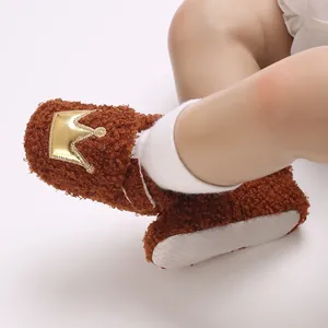 Close-up detail of brown fuzzy baby shoe featuring golden crown and soft non-slip sole