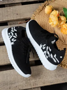 Close-up van zwart-witte gebreide sneakers op een rustieke houten ondergrond met bloemen.