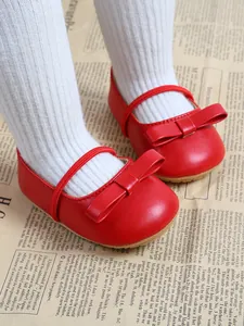 Close-up detail of red baby princess shoes with elegant bows and white ribbed tights.