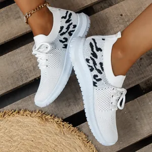 Detailopname van witte gebreide sneakers met luipaardprint op houten bodem