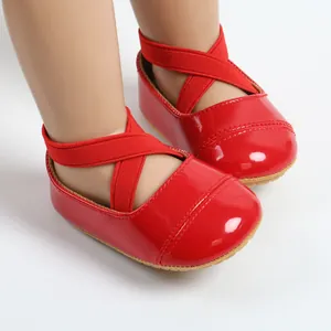 Close-up of shiny red baby princess shoes with cross-elastic straps and soft soles.