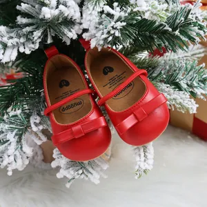 Festive red baby princess shoes with bows hanging on a snowy Christmas tree branch
