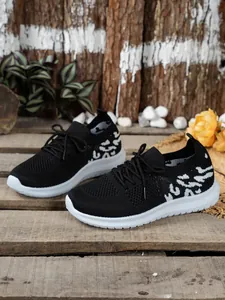 Detailweergave van zwarte fly-knit damessneakers met dikke witte zolen en luipaardprint