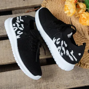 Detail van zwart-witte gebreide damessneakers met luipaardprint op rustiek hout