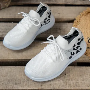 Detailoverzicht van witte gebreide damessneakers met luipaardprint op hout