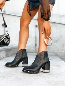 Detalle de botines negros bordados con tacón de cristal y suela decorada con tachuelas.