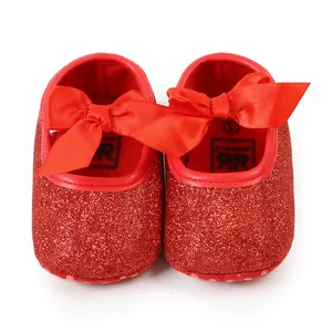 Close-up macro detail of red glittery baby shoes featuring decorative satin ribbon bows