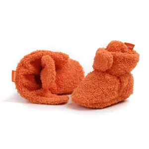 Dettaglio di babbucce in peluche arancione per neonati che mostra la morbida consistenza.