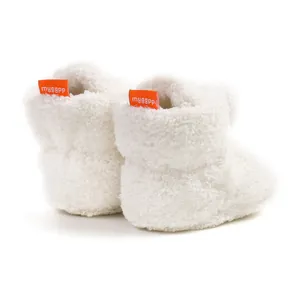 Dettaglio di scarpine bianche in peluche per neonato con etichetta arancione sul tallone