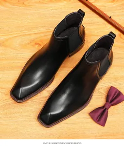 Vista superior de botas Chelsea de cuero negro sobre fondo de madera con pajarita