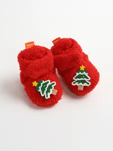 Dettaglio di scarpine neonato in peluche rosso con ricamo a forma di albero di Natale.