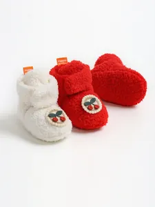 Dettaglio di scarpine invernali in peluche per neonati con motivi a ciliegia ricamati