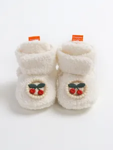 Primo piano di scarpine per neonati in peluche bianco spesso con ricamo a forma di ciliegia.