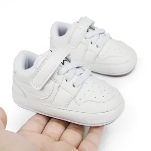 Close-up of small white infant walking shoes held in hand to show scale and soft material.