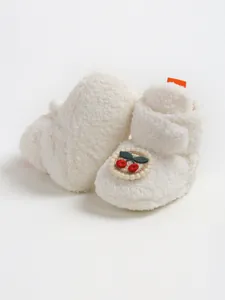 Dettaglio scarpine invernali in peluche bianco per neonati con toppa a ciliegia ricamata
