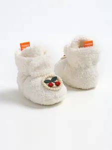 Dettaglio di scarpine per neonati in peluche bianca con toppa a ciliegia ricamata