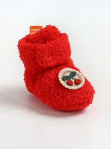 Dettaglio di uno stivaletto neonato rosso in peluche con graziosa toppa a ciliegia