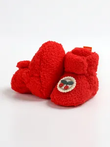Dettaglio di scarpine invernali in peluche rosso per neonati con patch ciliegia