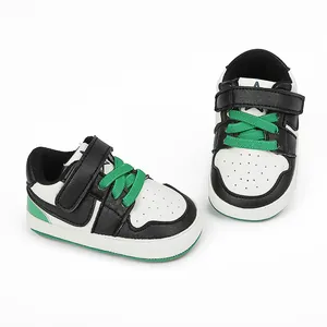Black and white baby sneakers with green laces and soft rubber soles for walking.