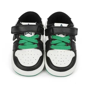 Front view of black and white baby sneakers with vibrant green laces and soft rubber soles