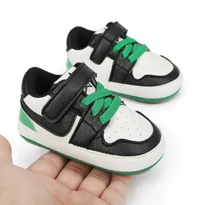 Detailed view of black and white baby sneakers with green laces held in hand for scale