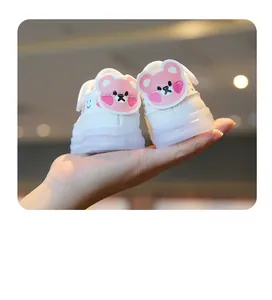 Gros plan de chaussures de marche blanches pour bébé avec ours rose et semelles lumineuses.