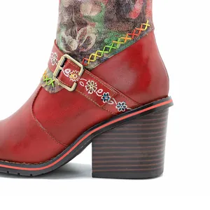 Gros plan d'une botte en cuir rouge à talon bloc avec coutures colorées et boucle florale