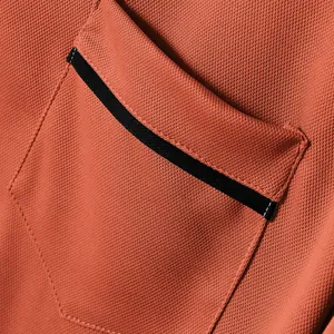 Macro shot showing the pique fabric texture and black-trimmed pocket on an orange polo shirt.