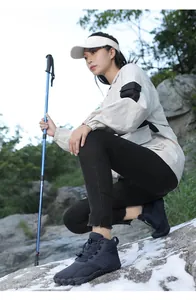 Female hiker in outdoor setting wearing navy blue mid-top winter snow boots on rock.