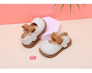 Detail view of baby girl cream leather Mary Jane shoes with brown suede bow and velcro strap.