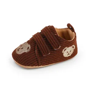 Detailaufnahme von braunen Cord-Babyschuhen mit Bärenstickerei und Klettverschluss.