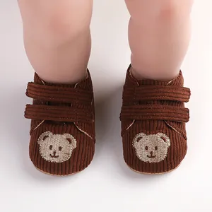 Nahaufnahme von braunen Baby-Lauflernschuhen aus Cord mit Bärenstickerei und Klett