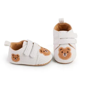 Detail of white corduroy baby walking shoes featuring cute brown bear embroidery