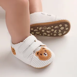 Close-up of white corduroy infant walking shoes with cute brown bear embroidery