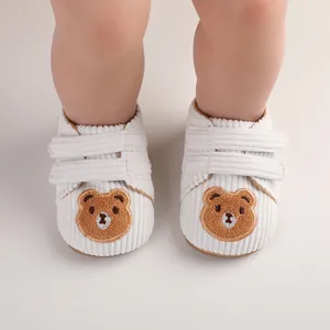 Close-up detail of white corduroy baby walking shoes featuring cute embroidered bear faces