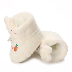 Gros plan de chaussons pour bébé en peluche blanche avec oreilles de lapin et carotte
