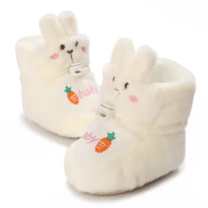 Détail de chaussons blancs en peluche pour bébé avec oreilles de lapin et carotte brodée
