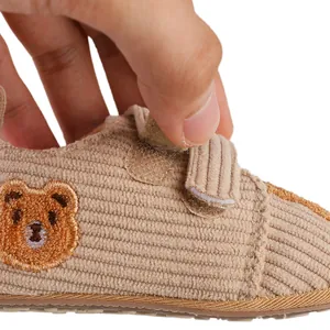Close-up of corduroy baby shoe with bear embroidery and adjustable velcro closure.