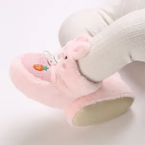 Gros plan de chaussons bébé en peluche rose avec oreilles de lapin et carotte brodée