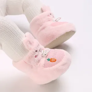 Gros plan de bottines bébé roses en peluche avec broderie carotte et semelle souple.