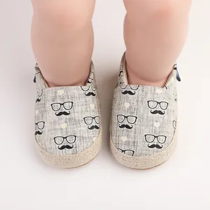 Detail von Baby-Lauflernschuhen mit Schnurrbart- und Brillenprint auf grauem Leinen