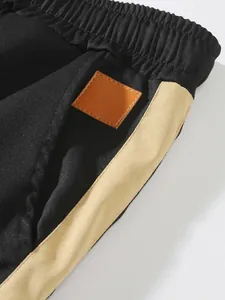 Detailed view of black cargo trousers featuring beige side stripe and leather patch