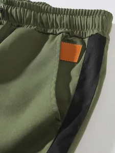 Macro detail of olive green men's cargo pants featuring a black side stripe and orange patch.