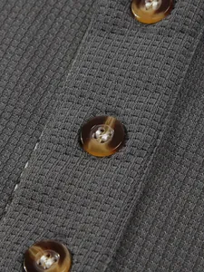 Nahaufnahme des grauen Waffelstrickgewebes und der Bernstein-Knöpfe am Herren-Poloshirt