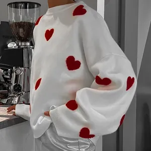Detailansicht eines weißen Strickpullovers mit roten Herzmustern und gerippten Bündchen