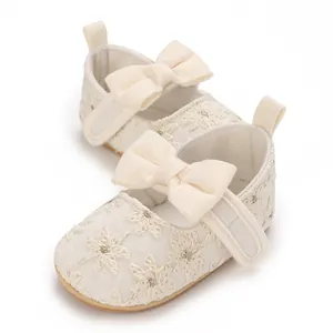 Gros plan de chaussures de princesse blanches pour bébé avec broderie et un grand nœud.