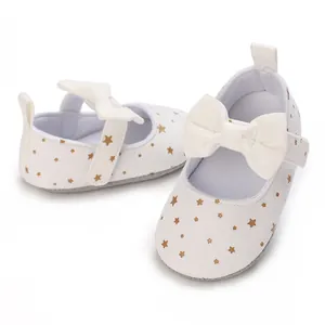Close-up of white baby girl walker shoes with gold star prints and decorative bow details.