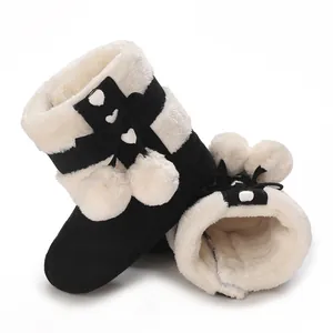 Close-up of warm black and white plush baby boots with decorative pom-poms and fleece lining