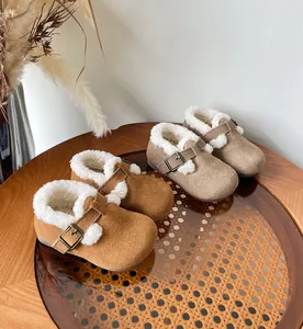 Cozy kids winter fleece-lined clogs in brown and beige colors on a rattan table.